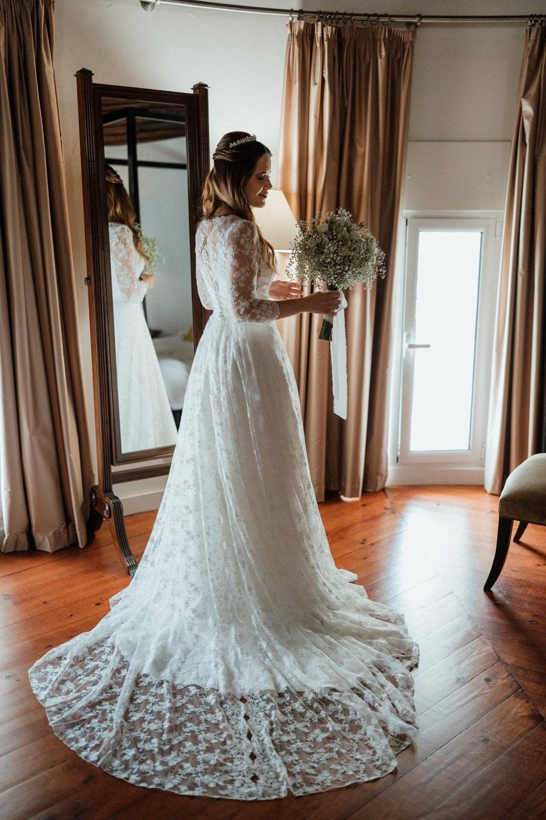 Noiva de costas, com a cauda do vestido de renda, frente ao espelho
