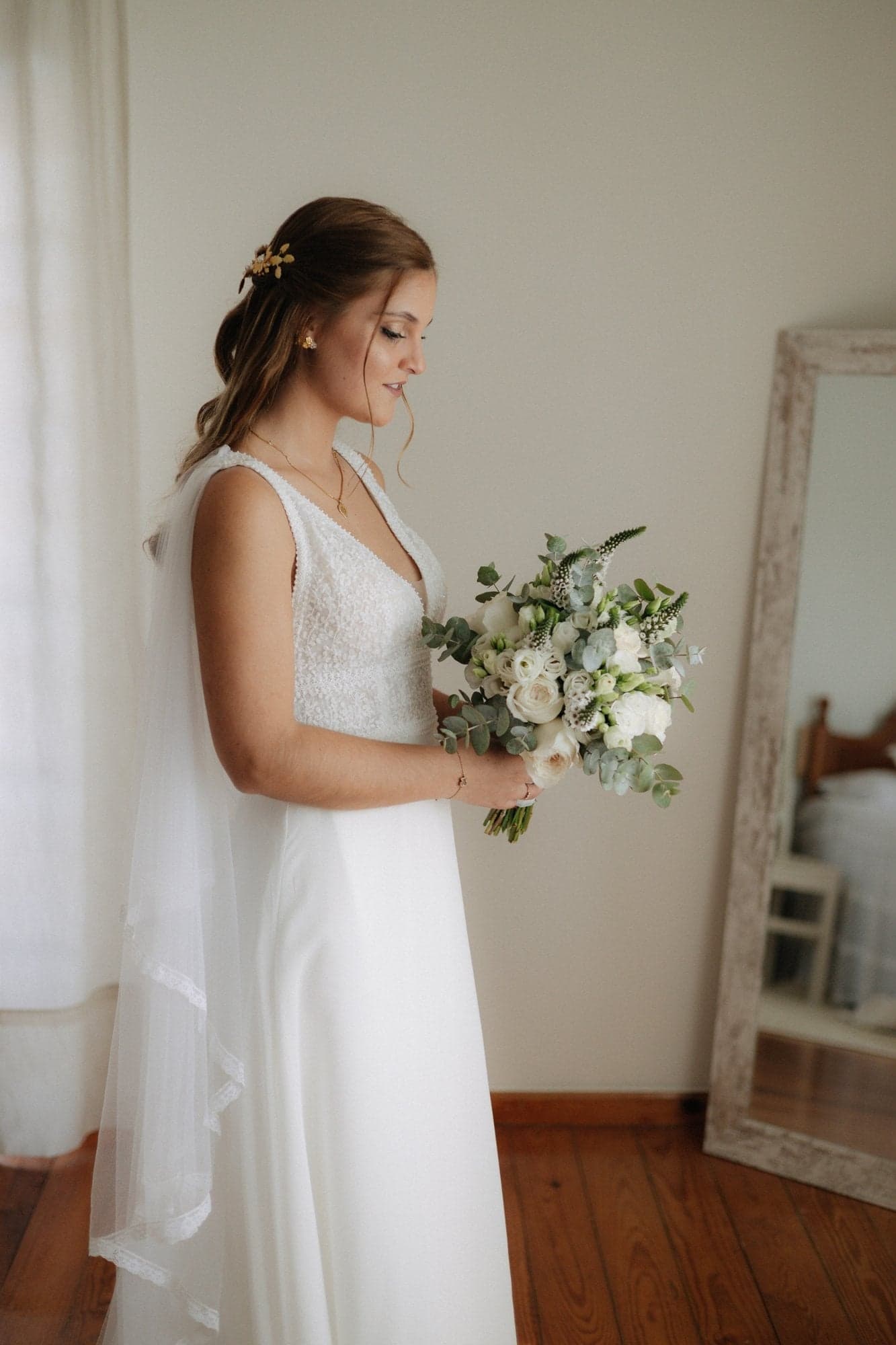 Noiva no quarto, de perfil, com o bouquet nas mãos